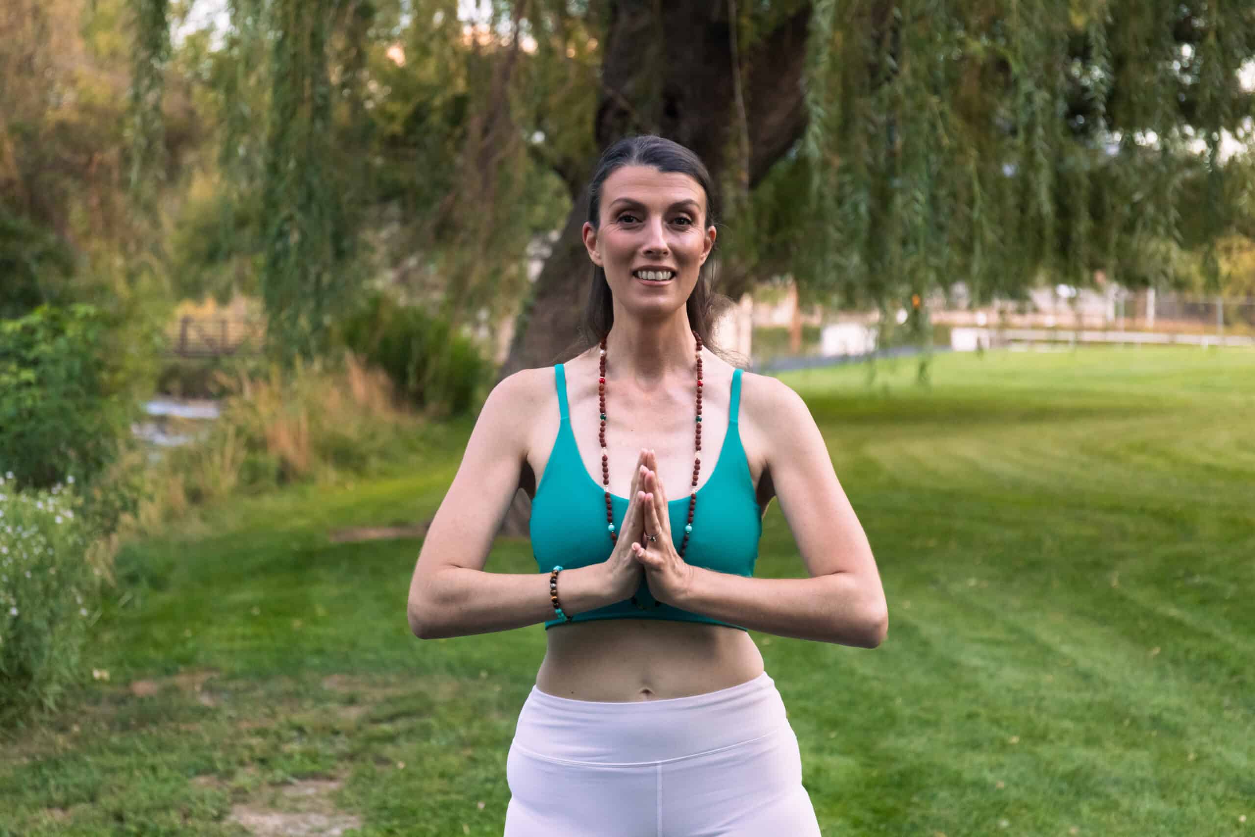 Danae Robinett practicing yoga outdoors with hands in namaste pose.