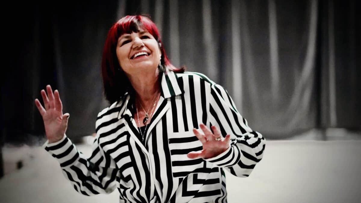 Gail Taylor, with red hair, laughing and gesturing, wearing a striped blazer.