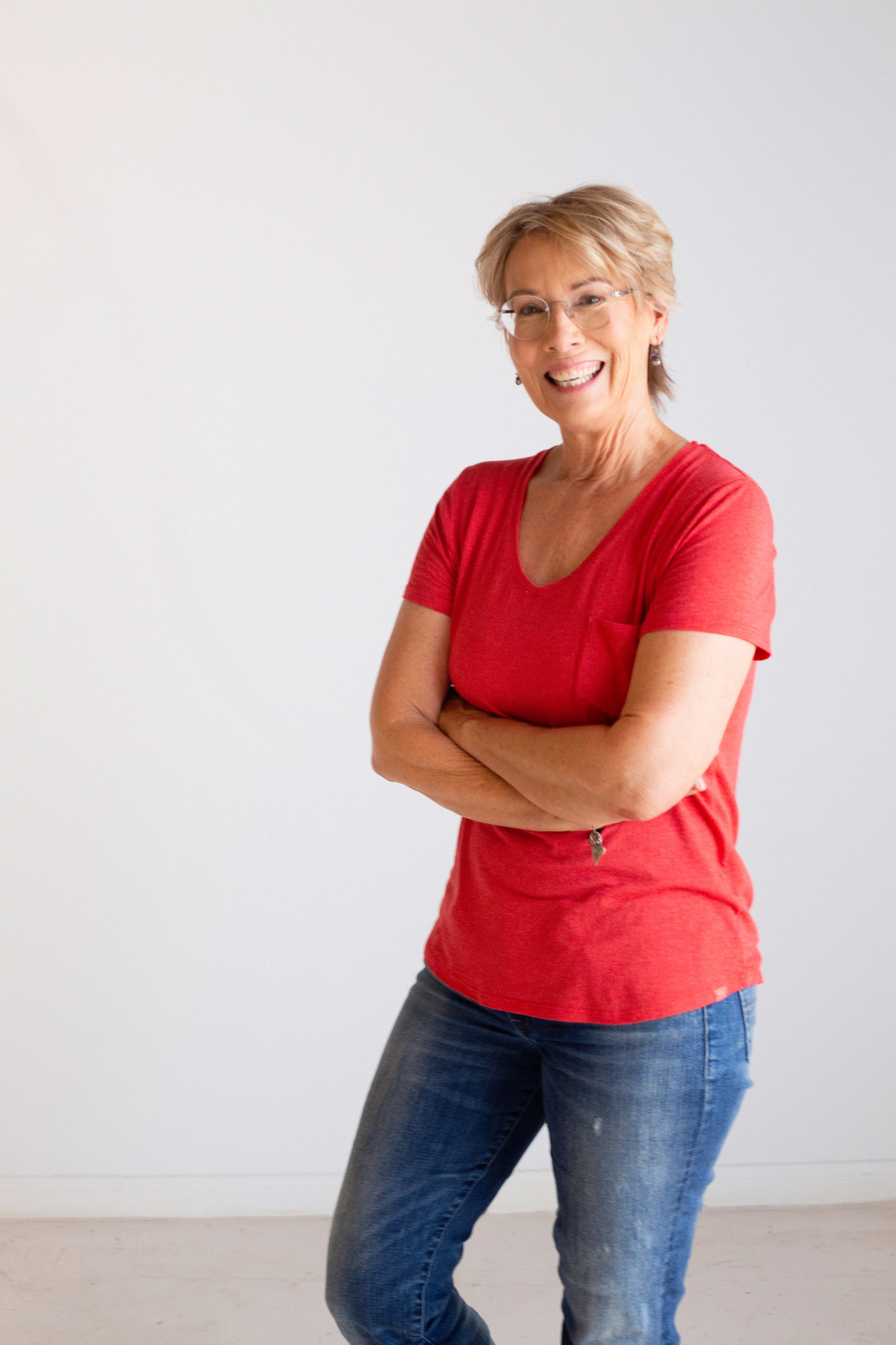 Kelly Howard smiling with glasses, wearing a red shirt and blue jeans, stands confidently with her arms crossed, embodying the role of community in fitness success.