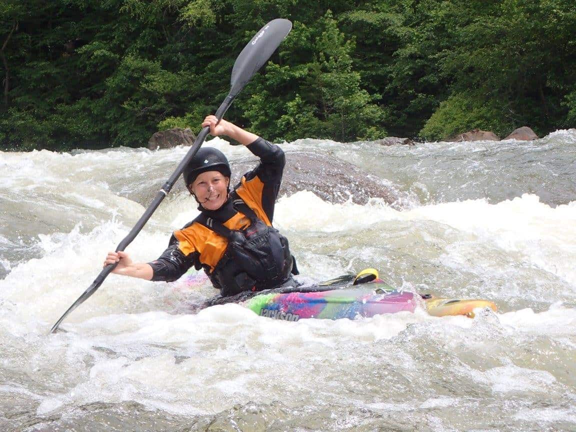 Kelly Howard kayaking through rough river rapids with a paddle raised.