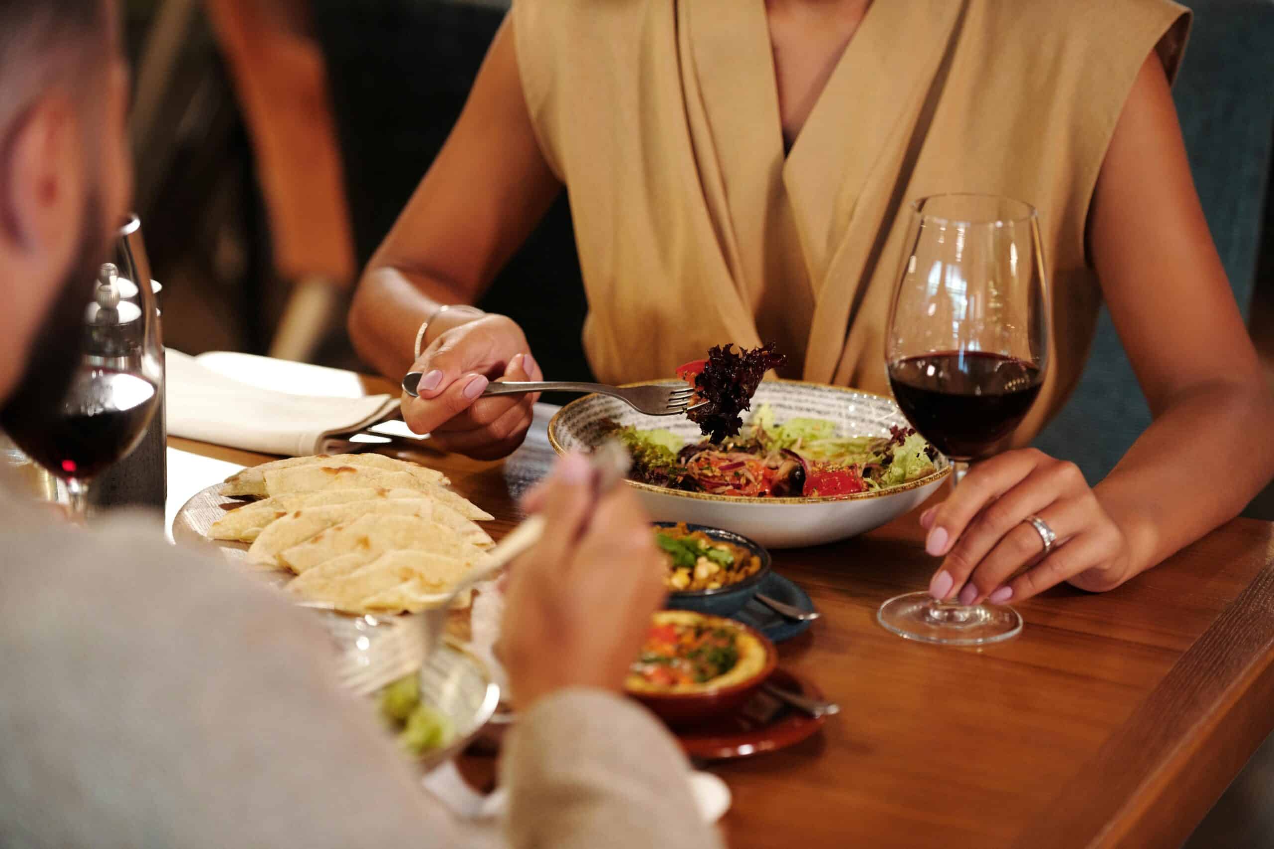 A couple rekindles connections over a healthy dinner, with a woman serving salad, surrounded by dishes and a glass of red wine.