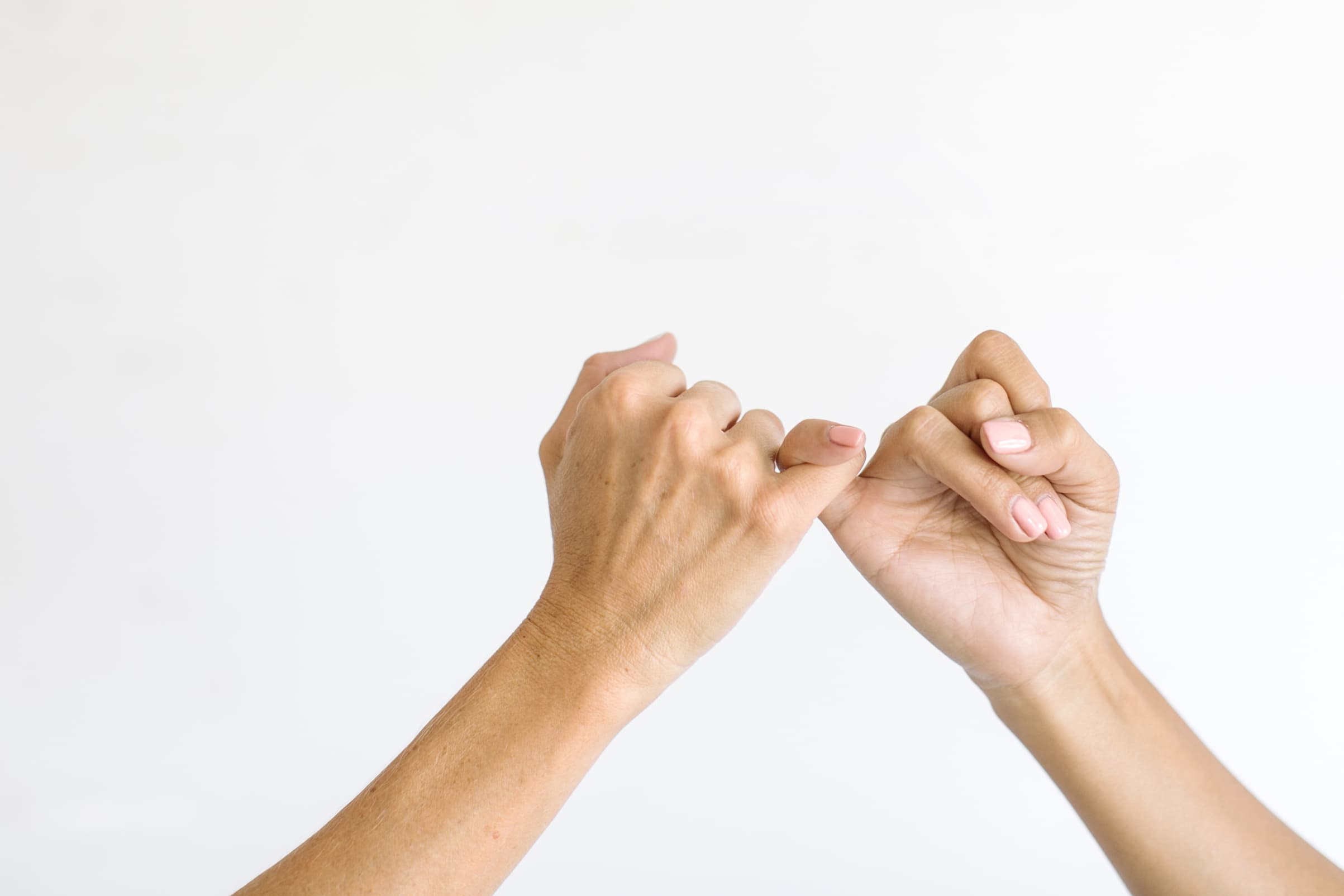 Two hands, embodying the strength found in community, making a pinky promise against a plain background.