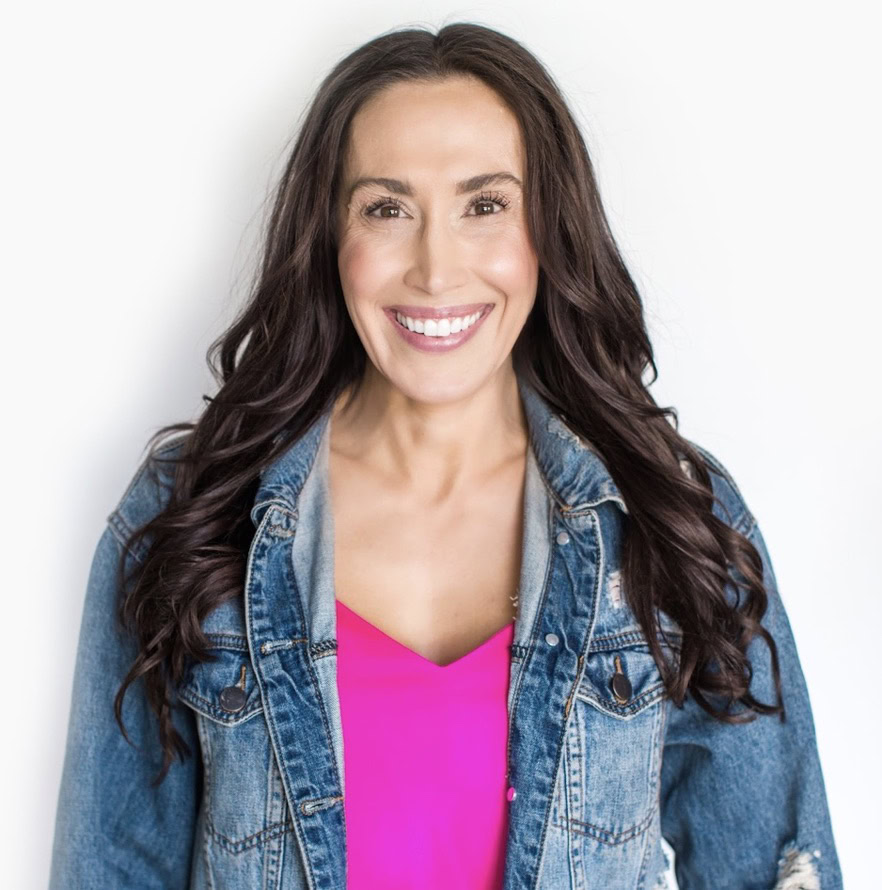 Dr. Anna Marie-Frank, with long, brown hair wearing a denim jacket over a pink top, smiles at the camera against a white background.