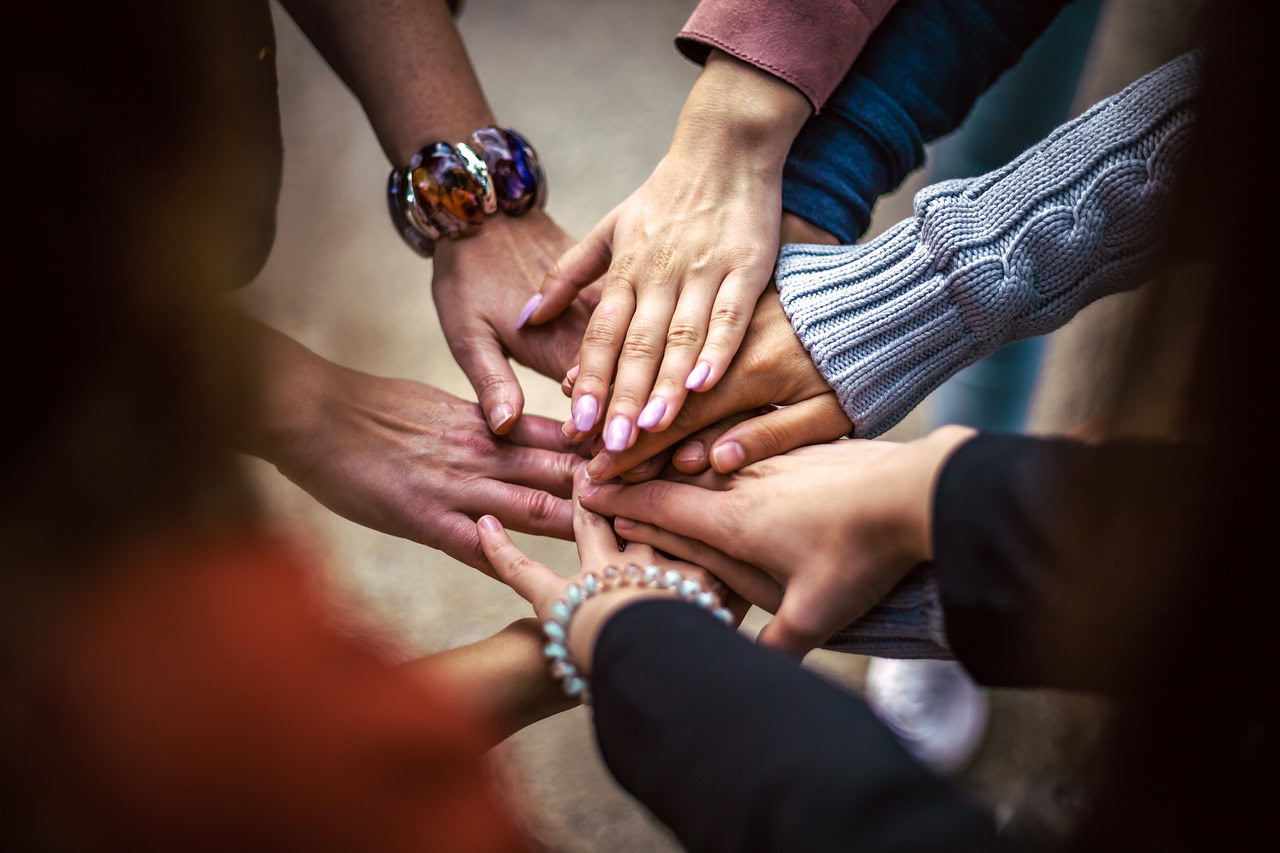 A close-up of multiple hands stacked together in a gesture of unity, community, and teamwork.