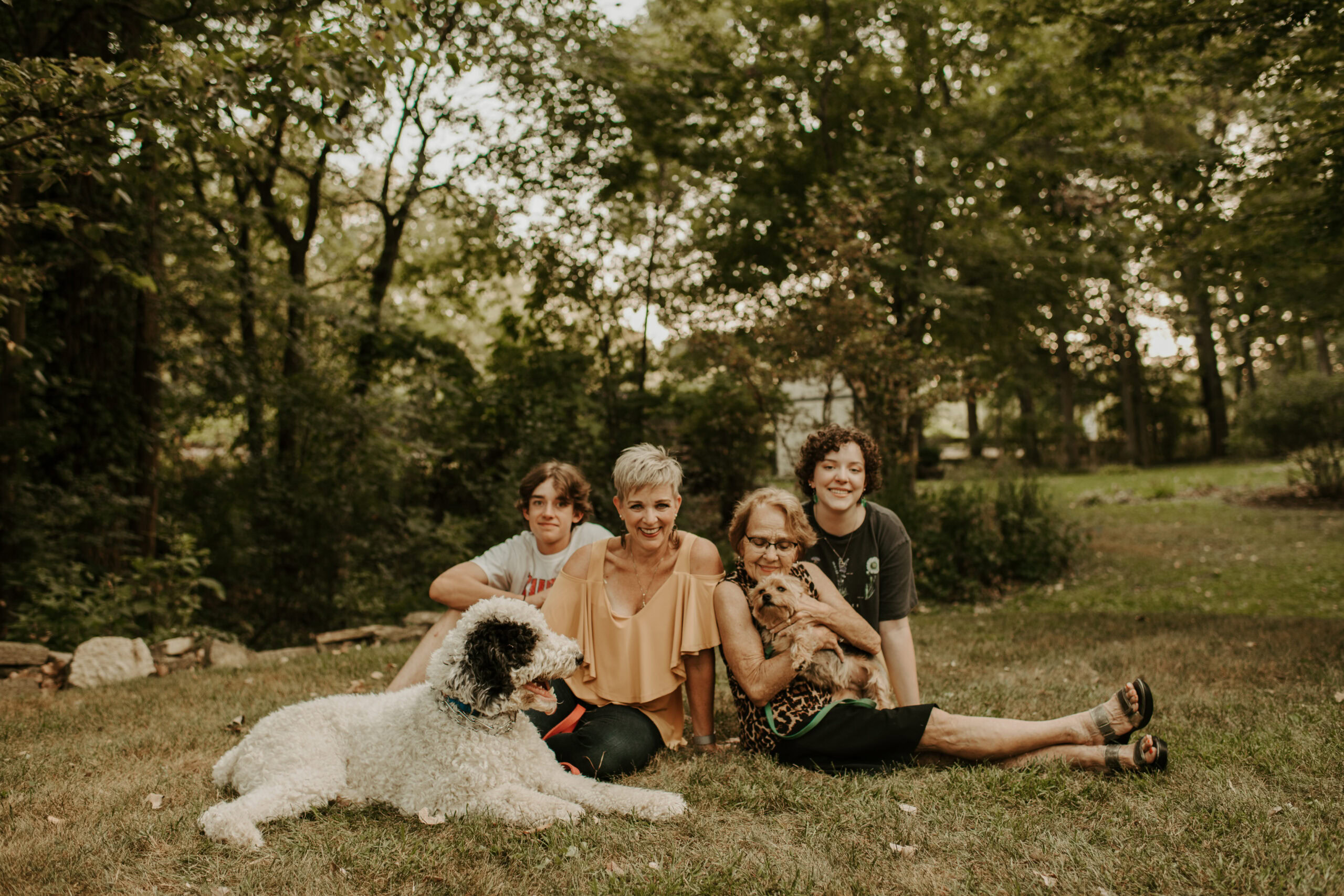 Dr. Kris's family, four people building a strong foundation of friendship sit on the grass with two dogs, surrounded by trees.