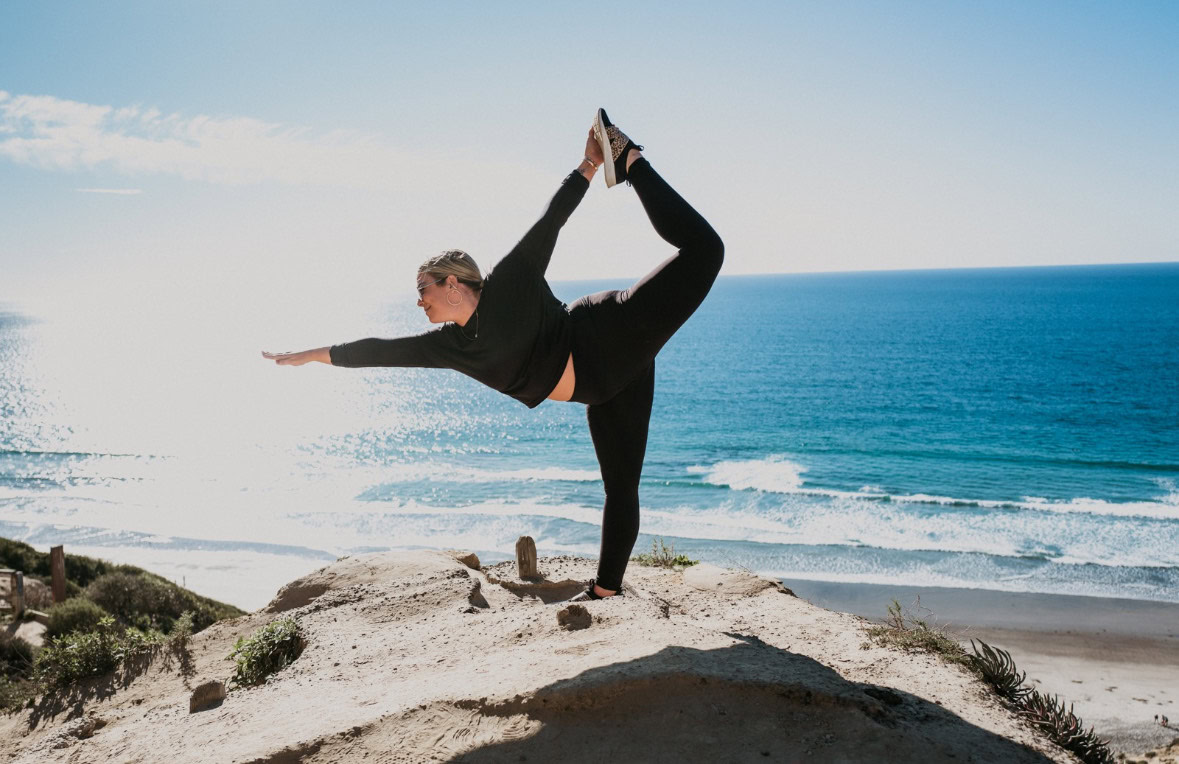 Megan McShane yoga pose on a rocky outcrop with the ocean in the background, emulating the serenity taught at Grace Yoga.