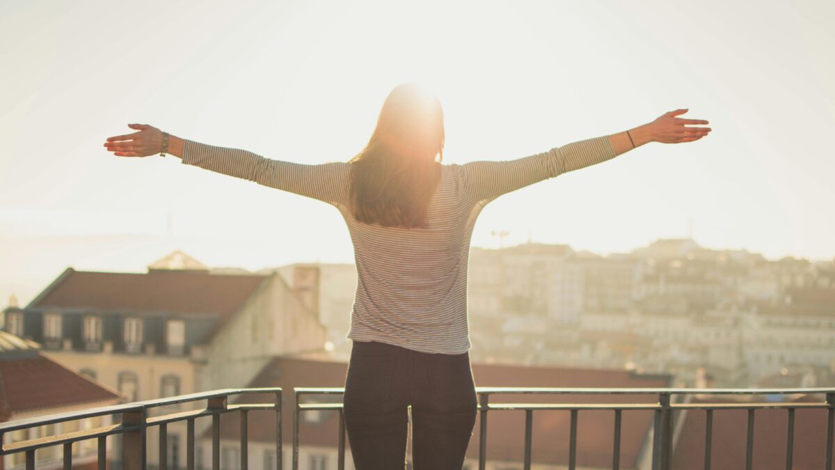 A person with outstretched arms stands on a balcony, facing the sunlit cityscape, leveraging life's lessons.