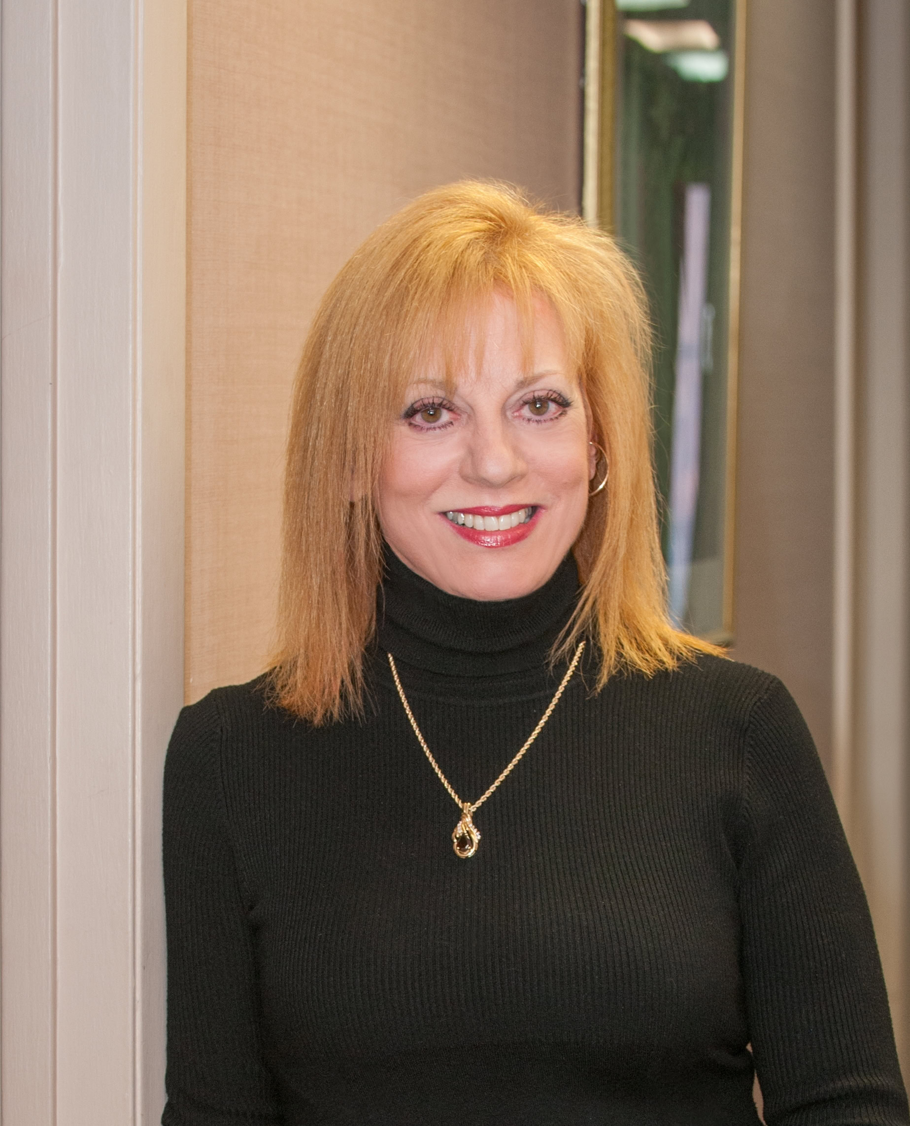 Upcoming Guest Dr. Emily Clionsky, a woman with shoulder-length blonde hair, wearing a black turtleneck sweater and a gold necklace, stands in front of a beige wall, smiling.