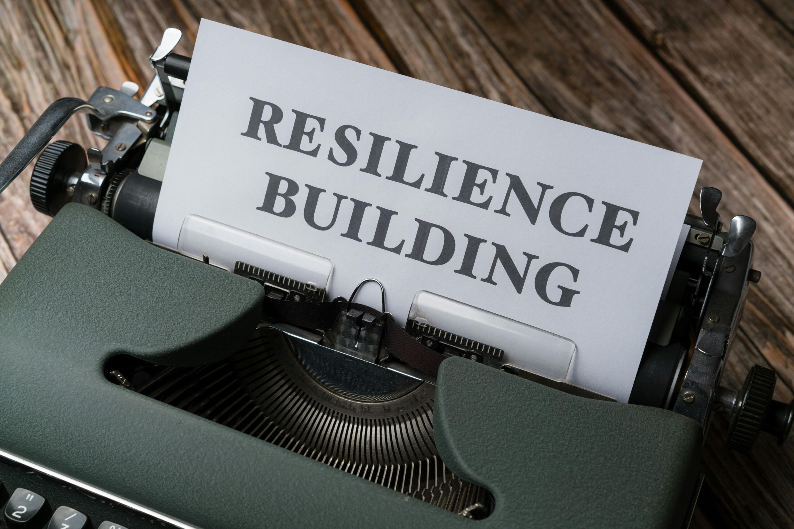 A typewriter displaying a sheet of paper with the words "RESILIENCE BUILDING" on it, redefining success. The typewriter is set on a wooden surface.