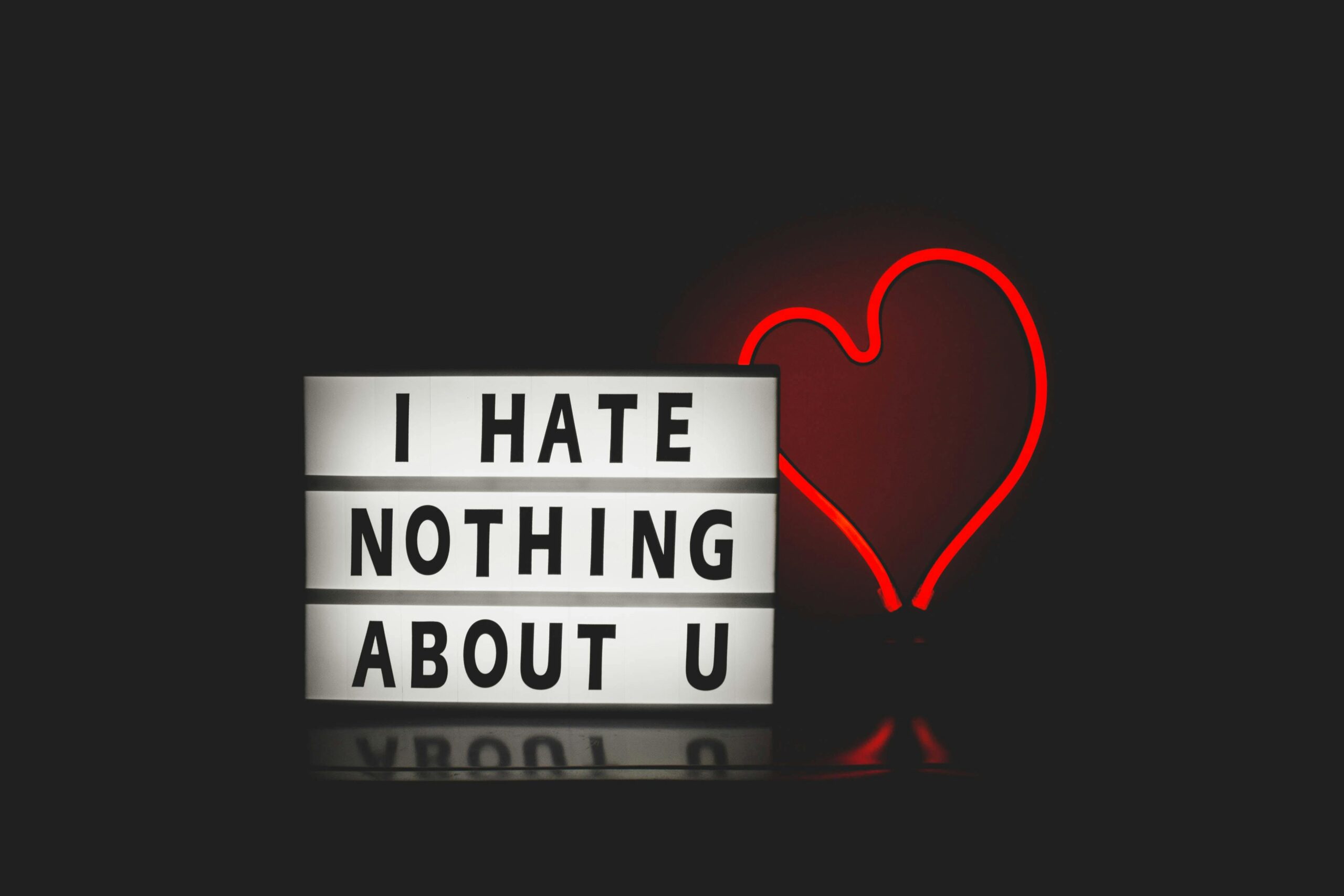 A lightbox sign with the message "I HATE NOTHING ABOUT U" next to a neon red heart on a black background, transforming negative thoughts into positive behavior.