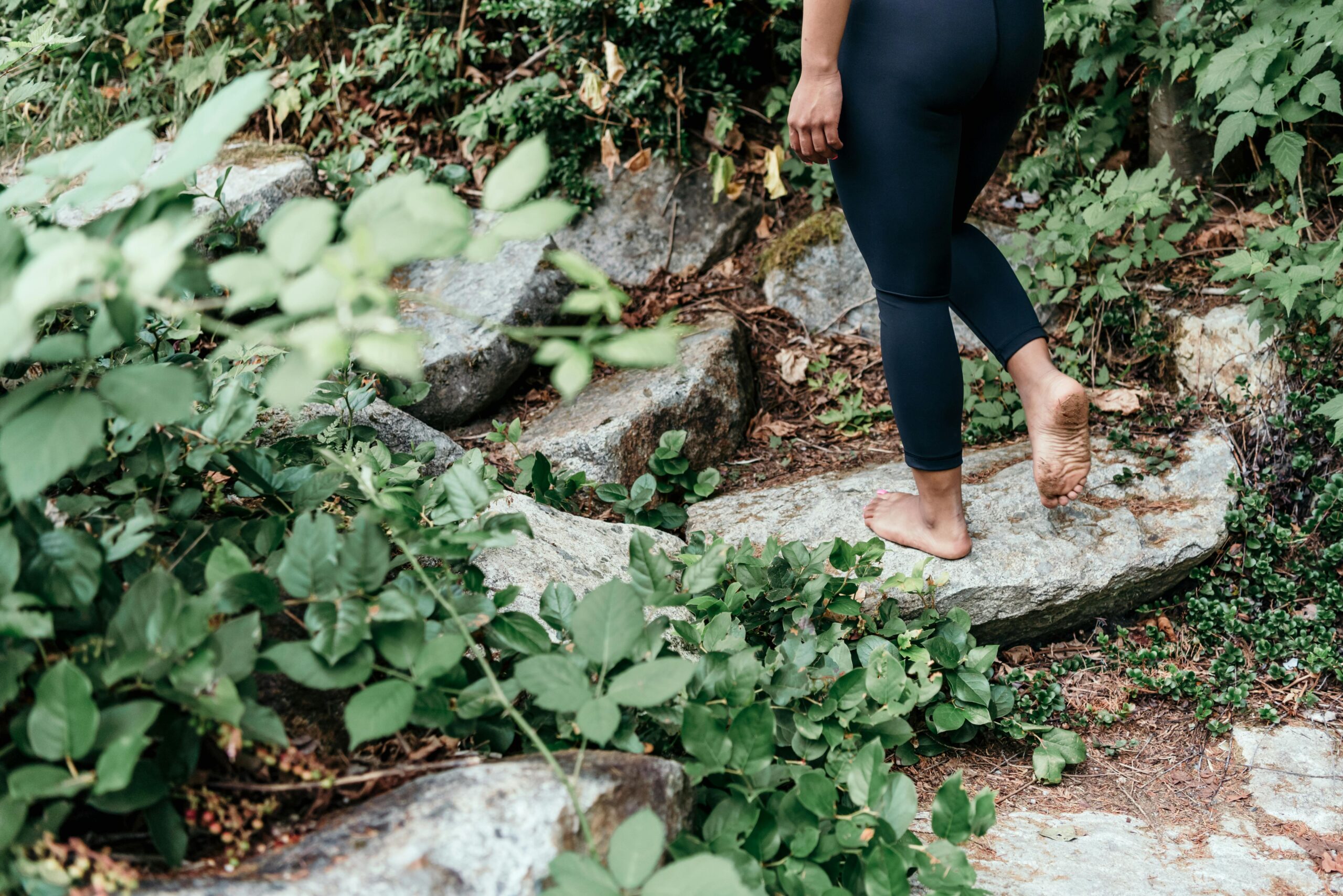 A person walking barefoot on stone steps in a lush, green, forested area embraces mindfulness practices.