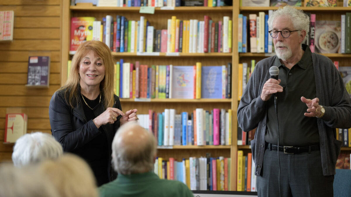 Dr. Emily Clionsky and Dr. Mitchell Clionsky in front of a group at a bookstore. One holds a microphone, discussing ways to reduce dementia risk, while the other gestures. Bookshelves filled with colorful books provide the perfect backdrop for this enlightening event.