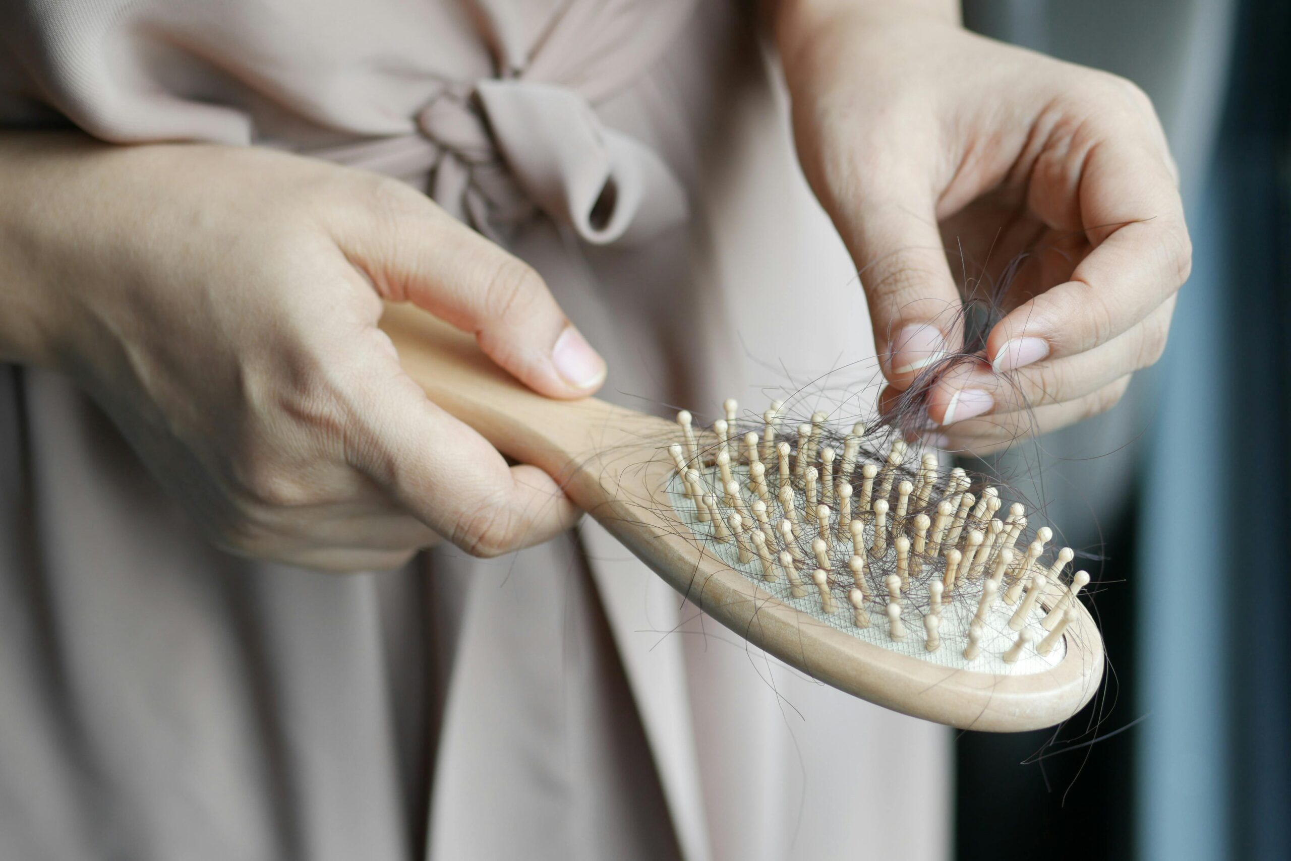 A person reflects on their personal journey while cleaning hair stuck in a wooden hairbrush with natural bristles, contemplating the challenges of hair loss.