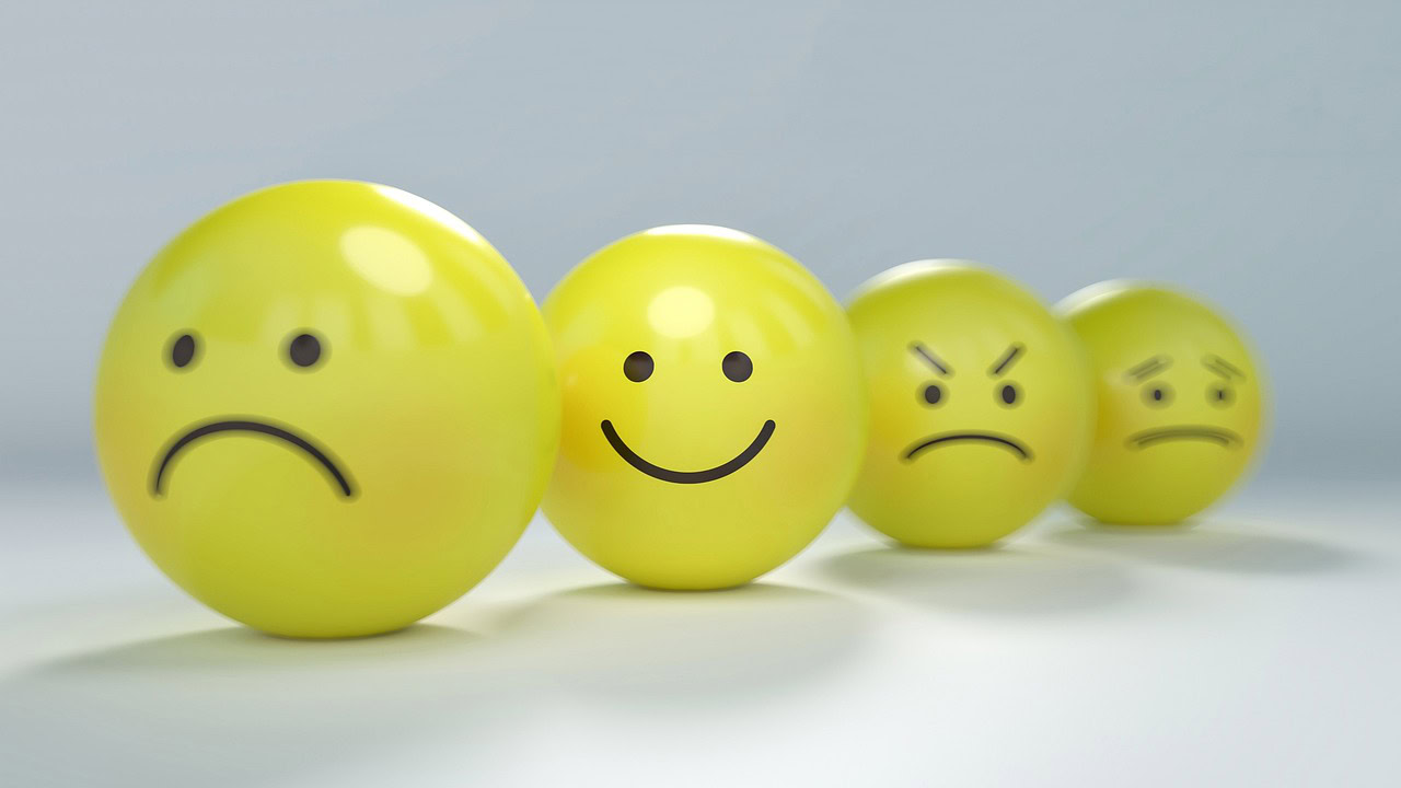 Four yellow balls, displaying unresolved emotions with expressions: sad, happy, angry, and frowning, are arranged in a row on a smooth surface.