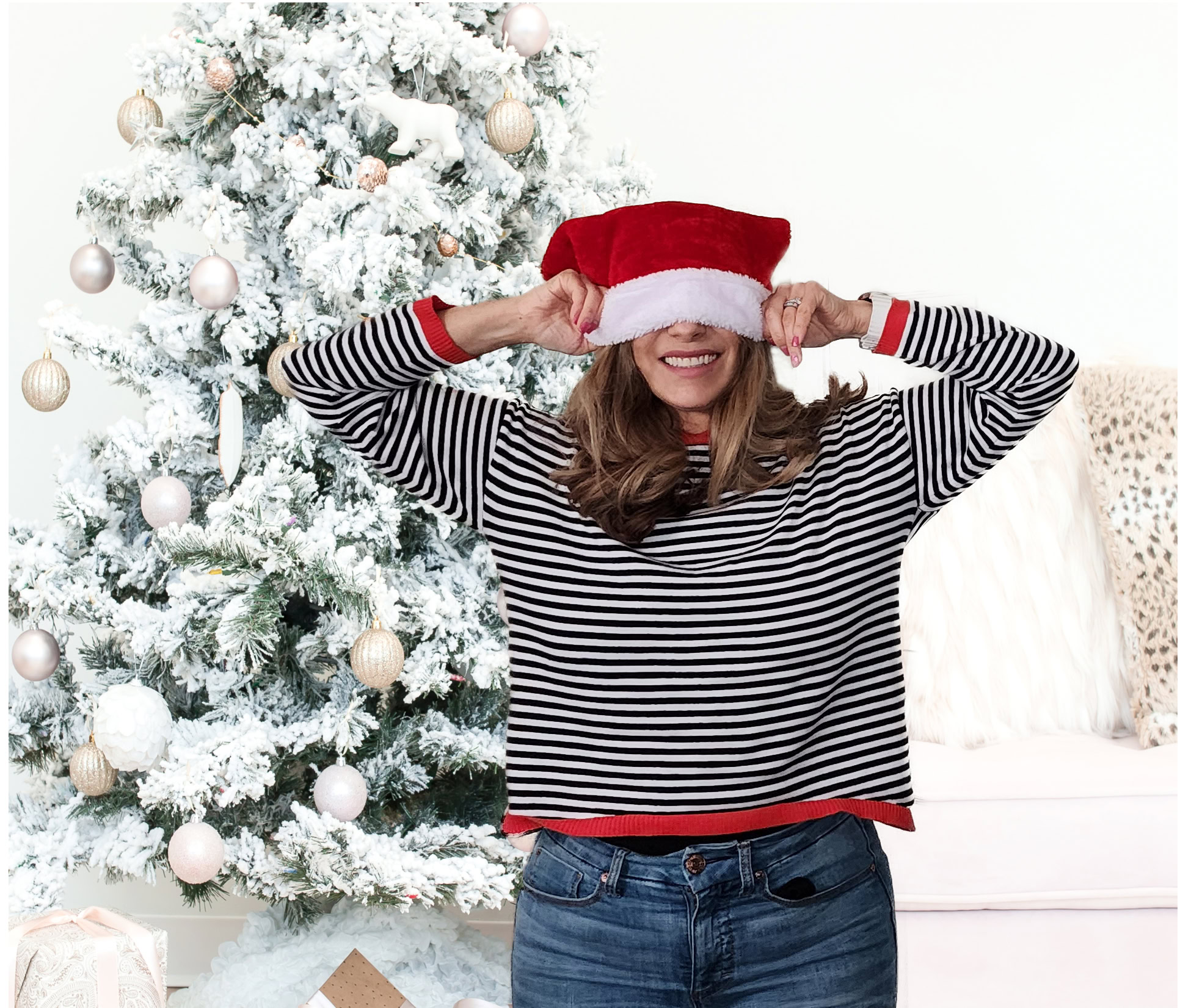 Carmen Hecox playfully covers their eyes with a Santa hat in front of a decorated Christmas tree, finding calm in the chaos of the holidays.