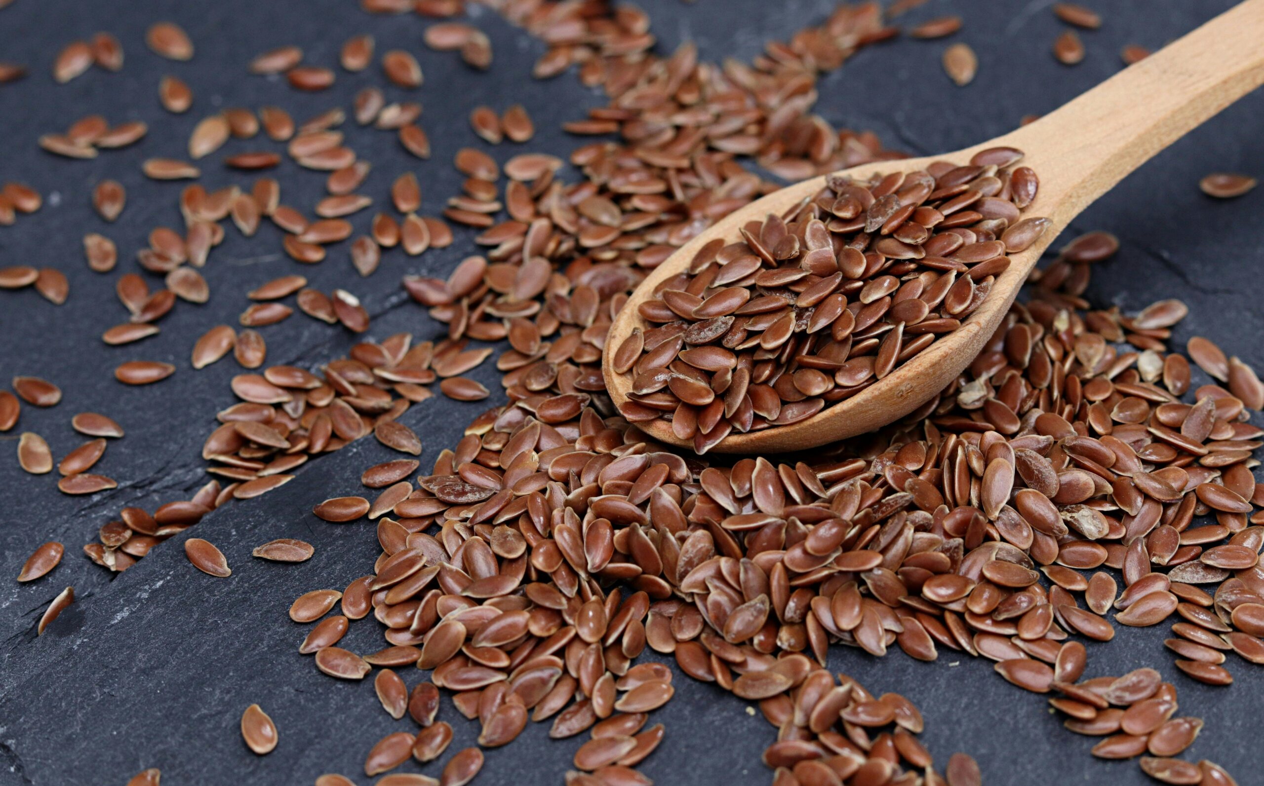 A wooden spoon on a dark surface, surrounded by scattered brown flaxseeds, hints at the promise of healthy oils.