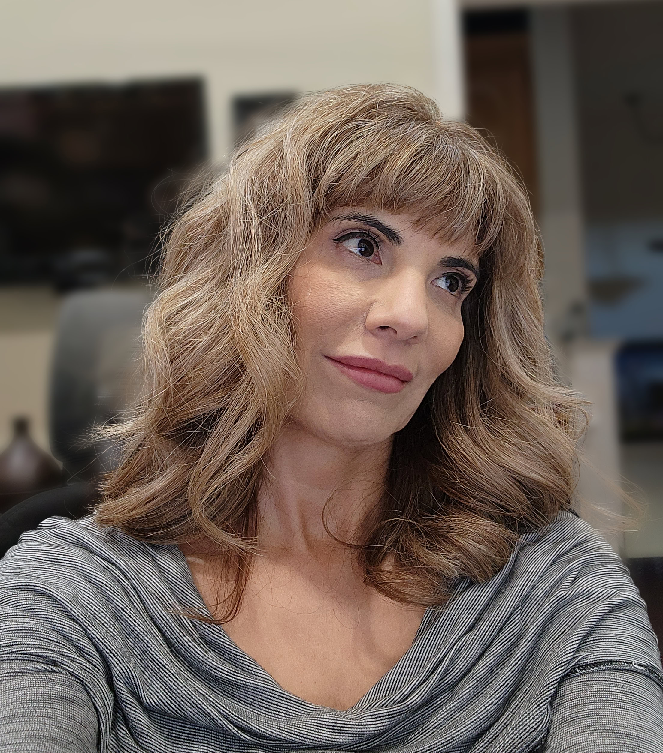 Carmen Hecox with wavy, medium-length hair that appears stronger during menopause, wearing a gray top and looking off-camera.