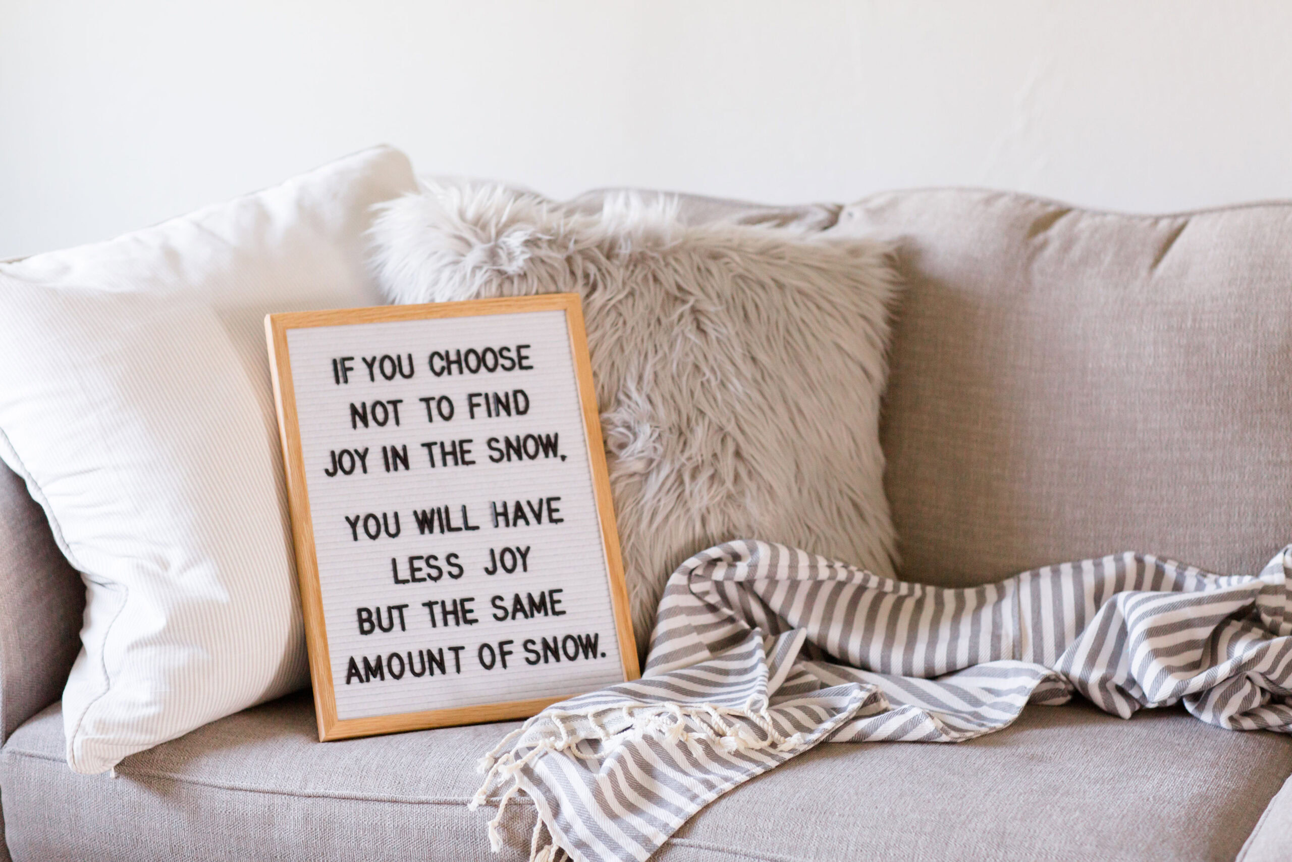 A letter board with the message about finding joy in vulnerability and the snow is placed on a beige couch with pillows and a striped blanket.