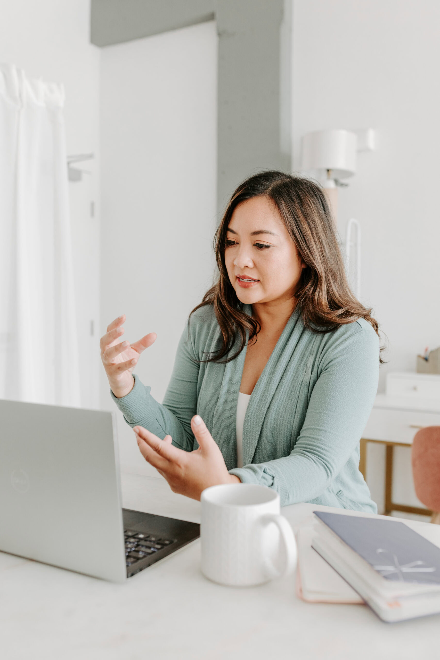 Dr. Val Cacho in a green cardigan sits at a desk with a laptop, gesturing as she discusses sleep aids. A mug and notebooks are on the table, emphasizing her dedication to understanding sleep apnea solutions.