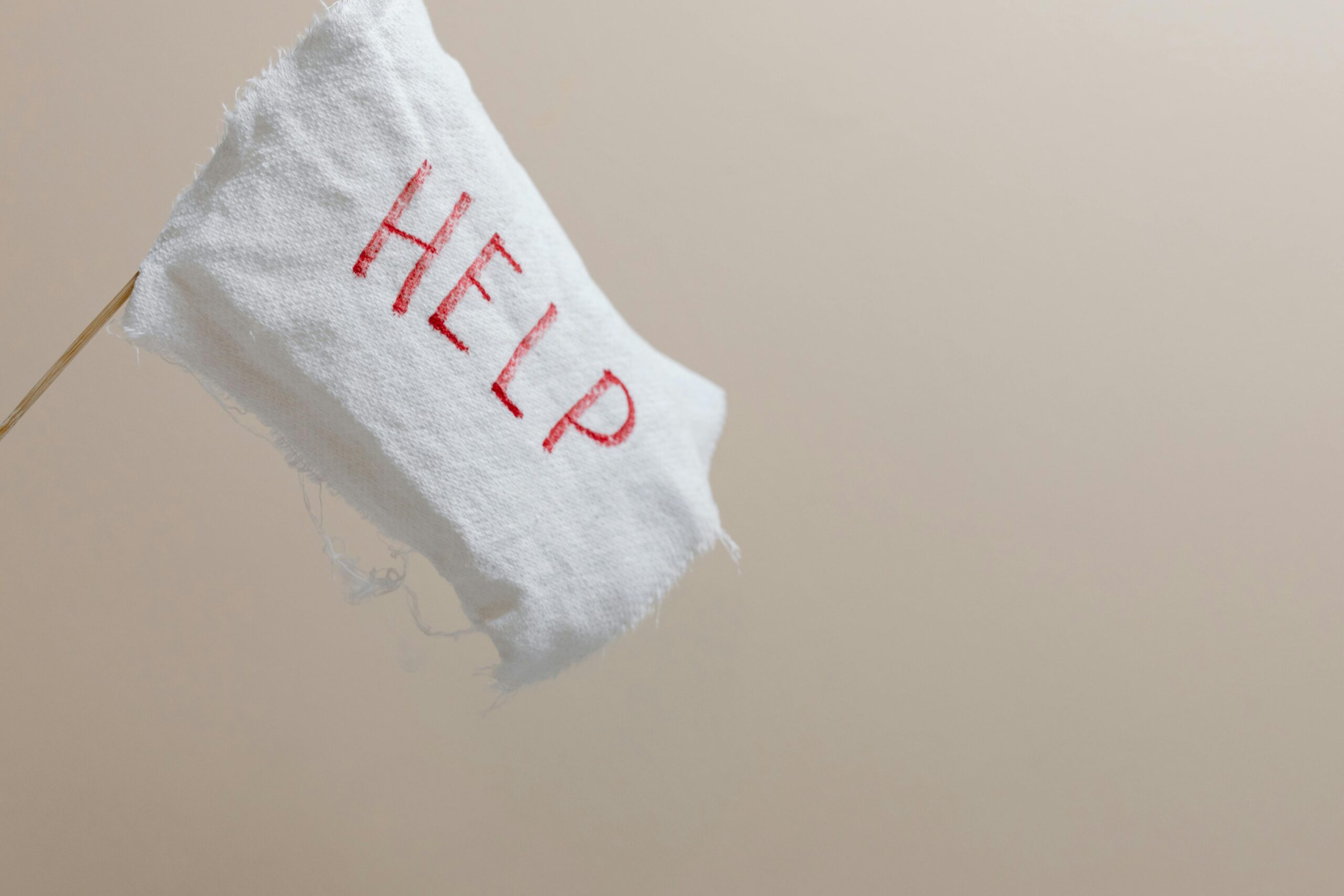 A white fabric flag with the word "HELP" stitched in red, set against a plain beige background, serves as a stark symbol for confronting life’s emergency scenarios.