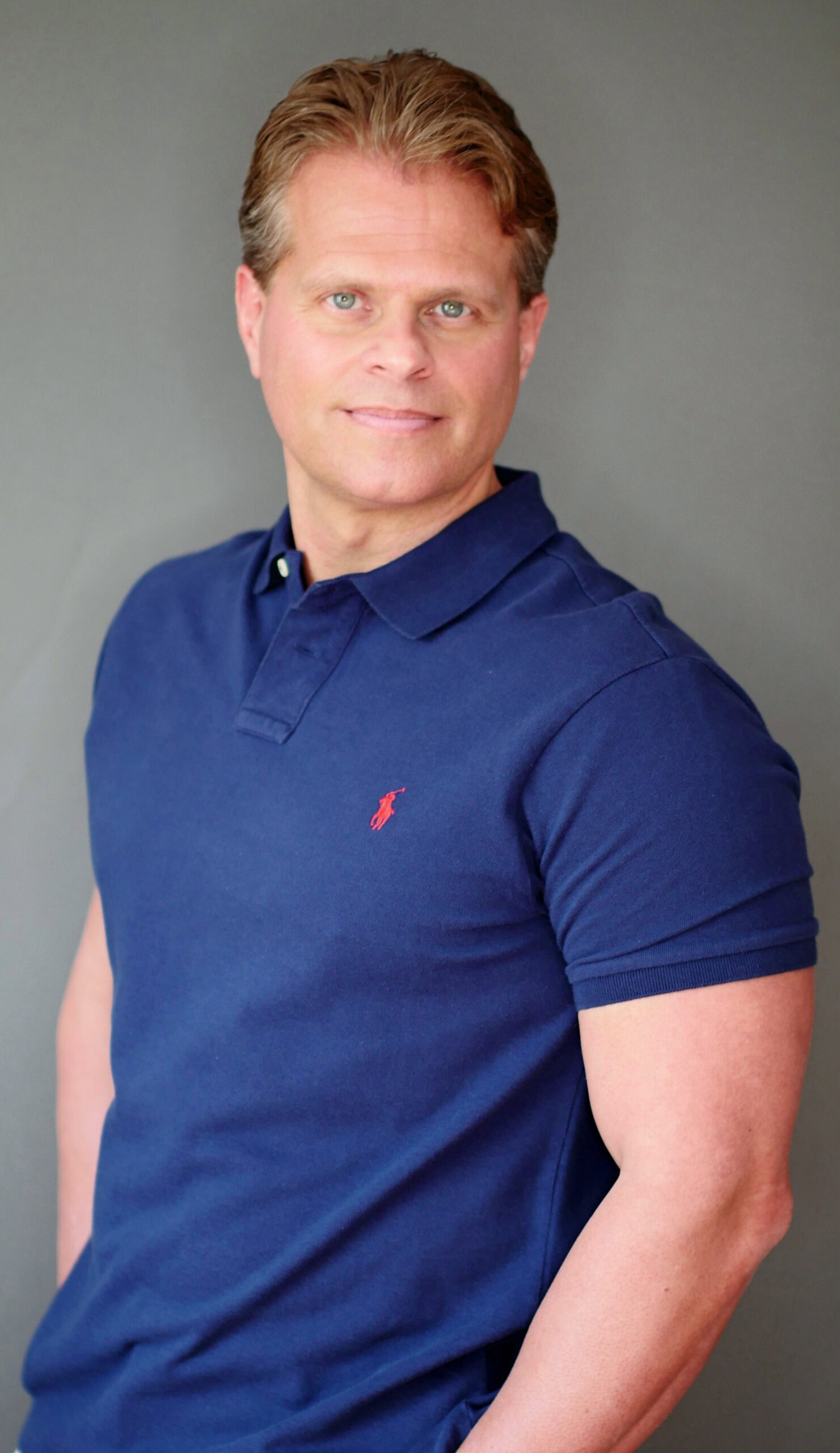 Dr. John Lewis in a navy blue polo shirt stands against a plain background, embodying balance like the science of sustainable weight loss.