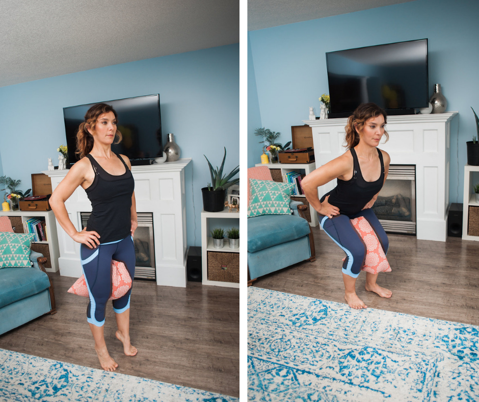 A woman in workout attire demonstrates surprising strength as she performs a knee lift exercise in her living room, holding a pillow between her knees. She stands confidently in front of a white fireplace and a TV, embracing strength over 50 with each movement.