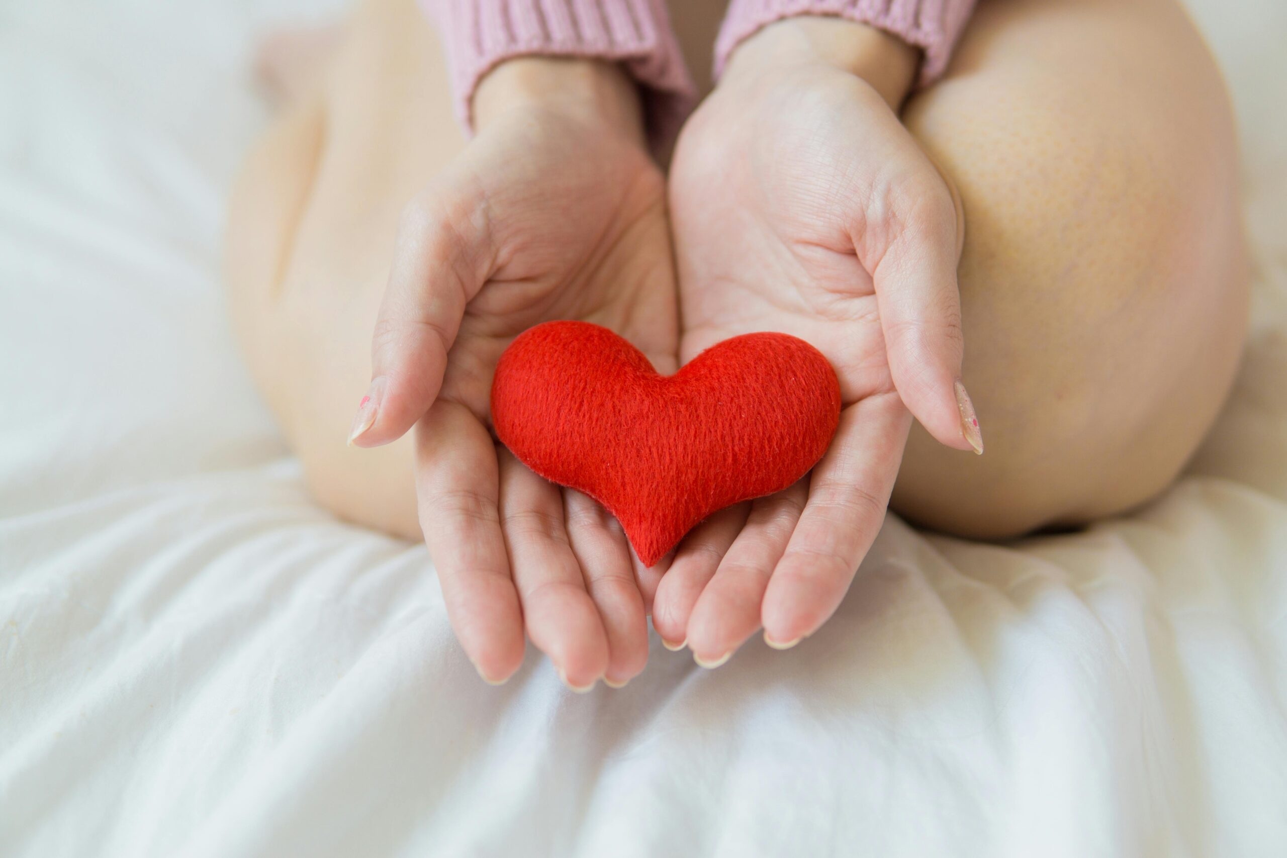 Hands gently cradle a red heart-shaped object while seated on white fabric, reflecting the importance of heart health during menopause.