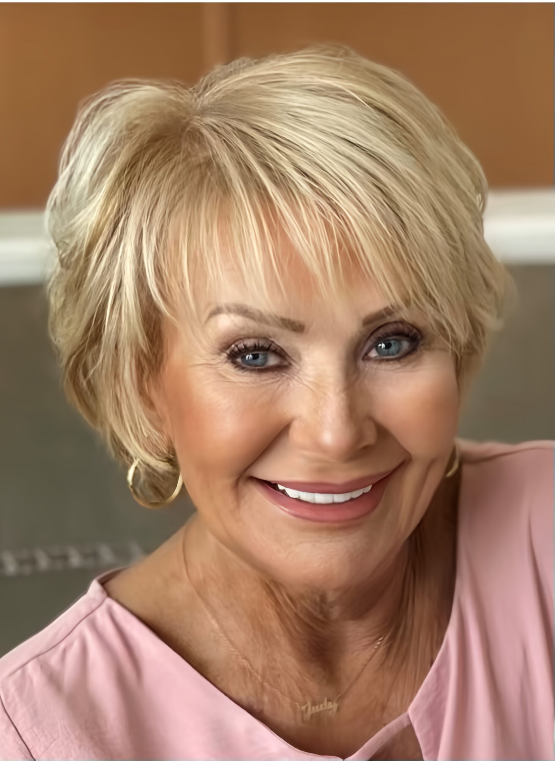 Upcoming Guest's Judy Henderson, a smiling woman with short blonde hair and hoop earrings, dons a vibrant pink top.