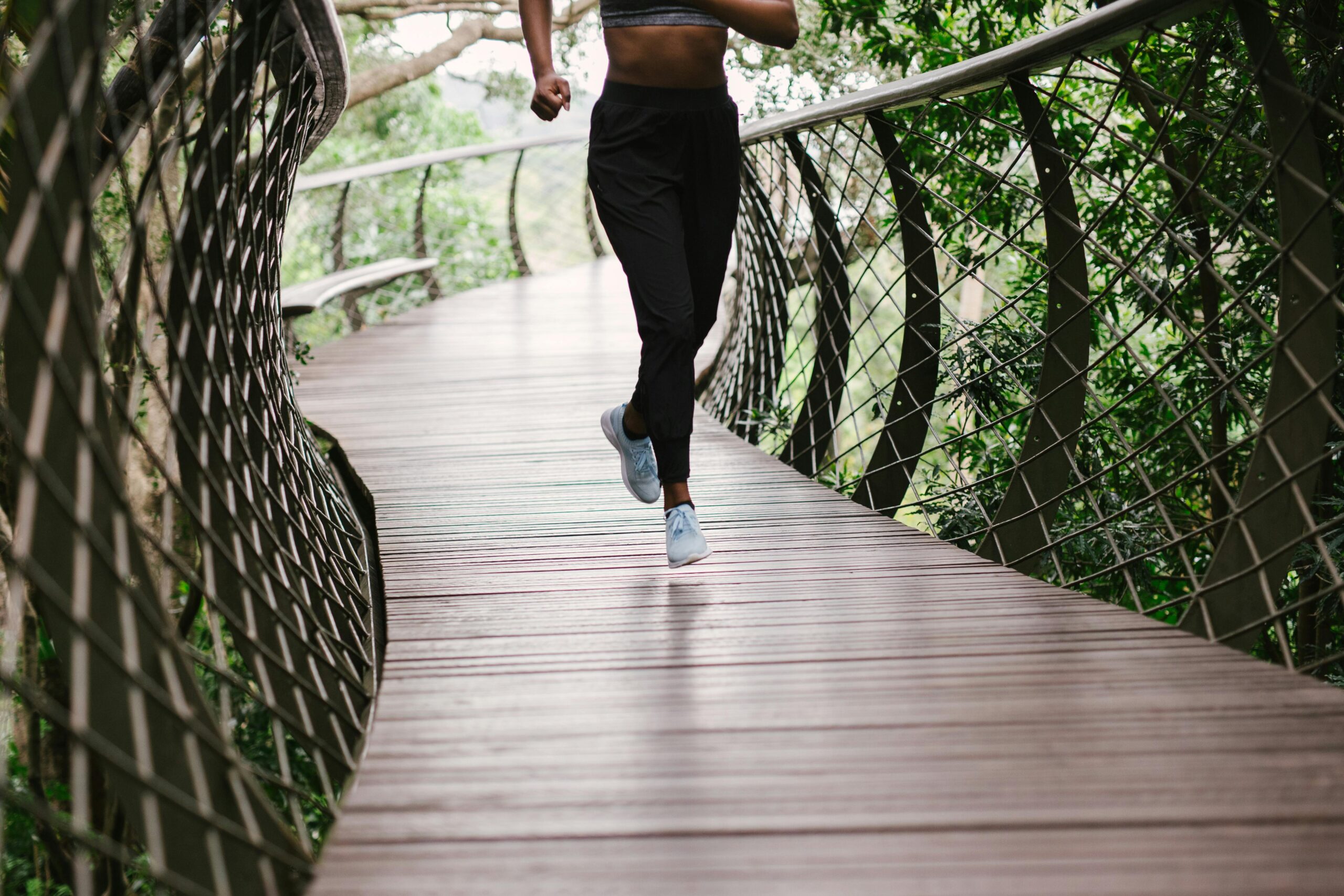 Person jogging on a curved wooden walkway surrounded by greenery, their lower body visible—capturing My Personal Journey: Embracing Change and Growth with every stride.