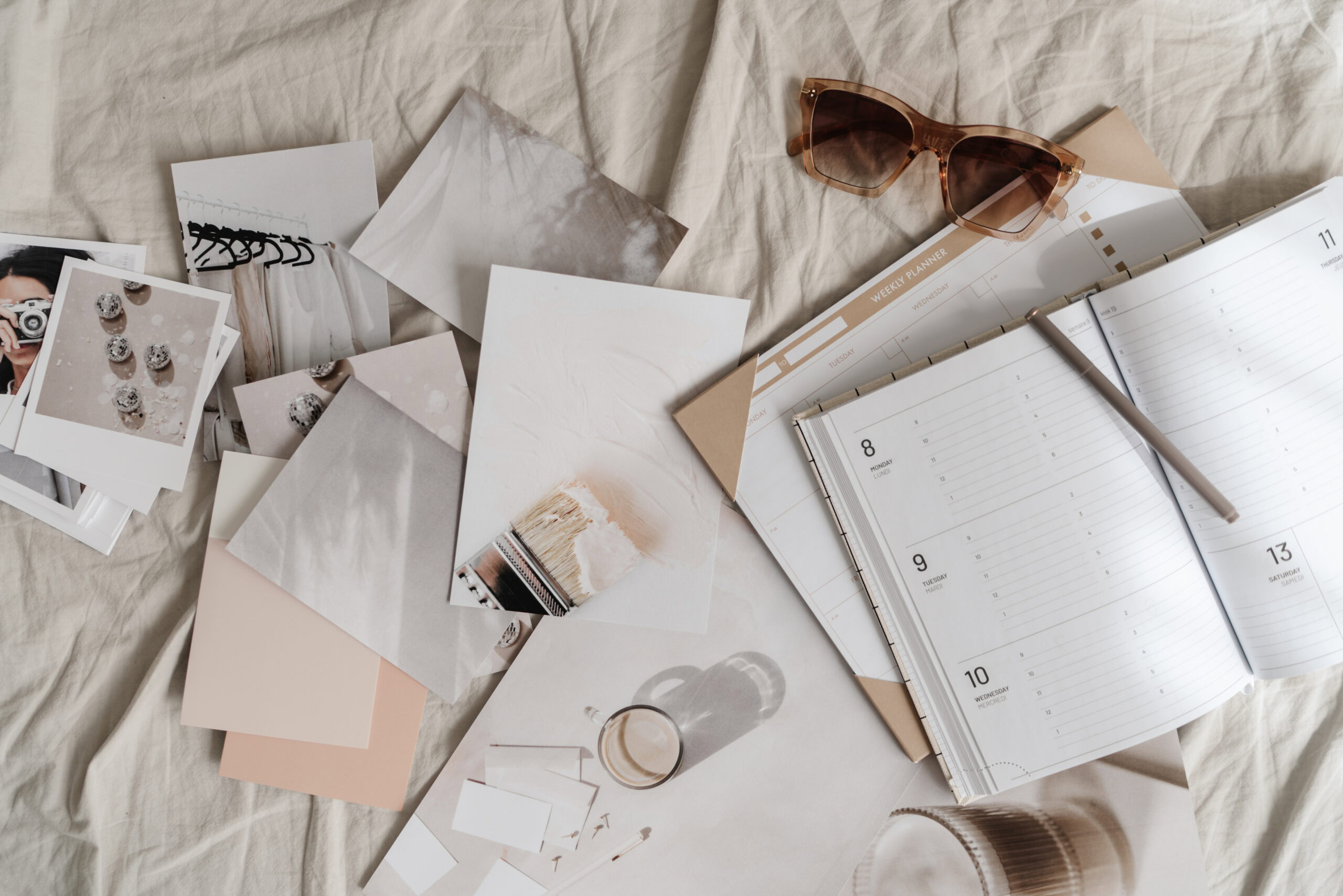 A planner, pen, eyeglasses, and assorted photos and color swatches are arranged on a beige fabric surface, inspiring you to strategically prioritize your goals.