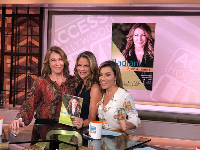 Three women sit at a table on a TV set with a poster and book titled "Radiant Again & Forever," smiling at the camera, as they discuss debunking the cancer myth.