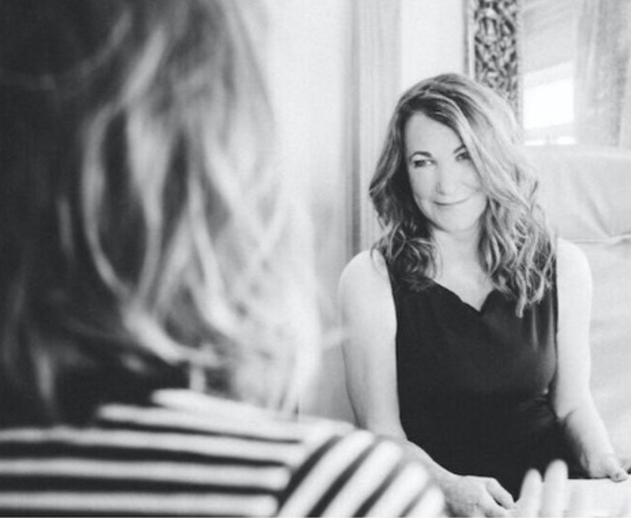 A woman with wavy hair in a sleeveless dress sits and looks at her reflection in a mirror, suggesting self-reflection—a reminder that individualized care is the key to hormone health. The image is in black and white, focusing on her head and shoulders.